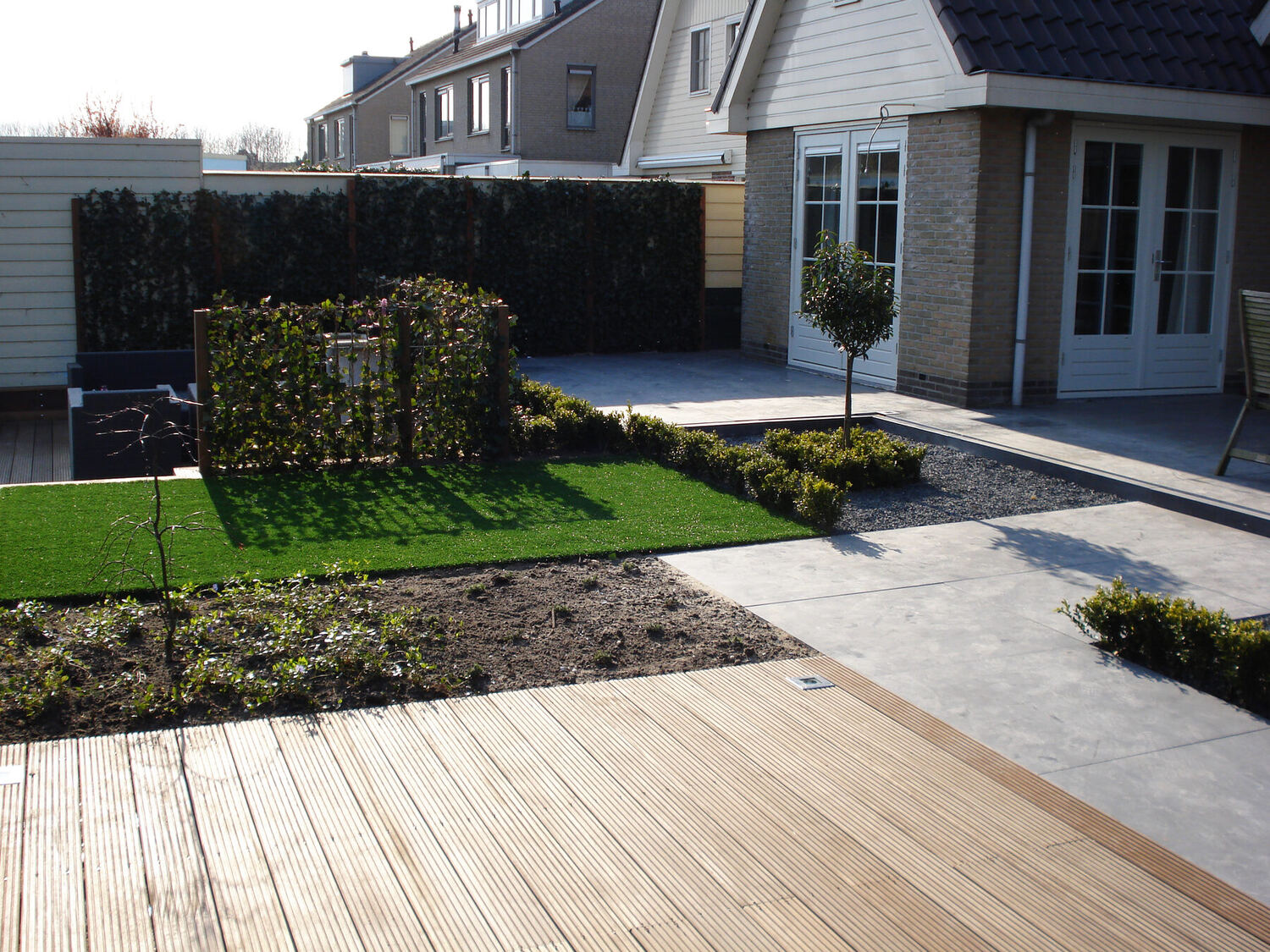 Tuin met houten vlonder en een verhoogd kunstgrasvlak