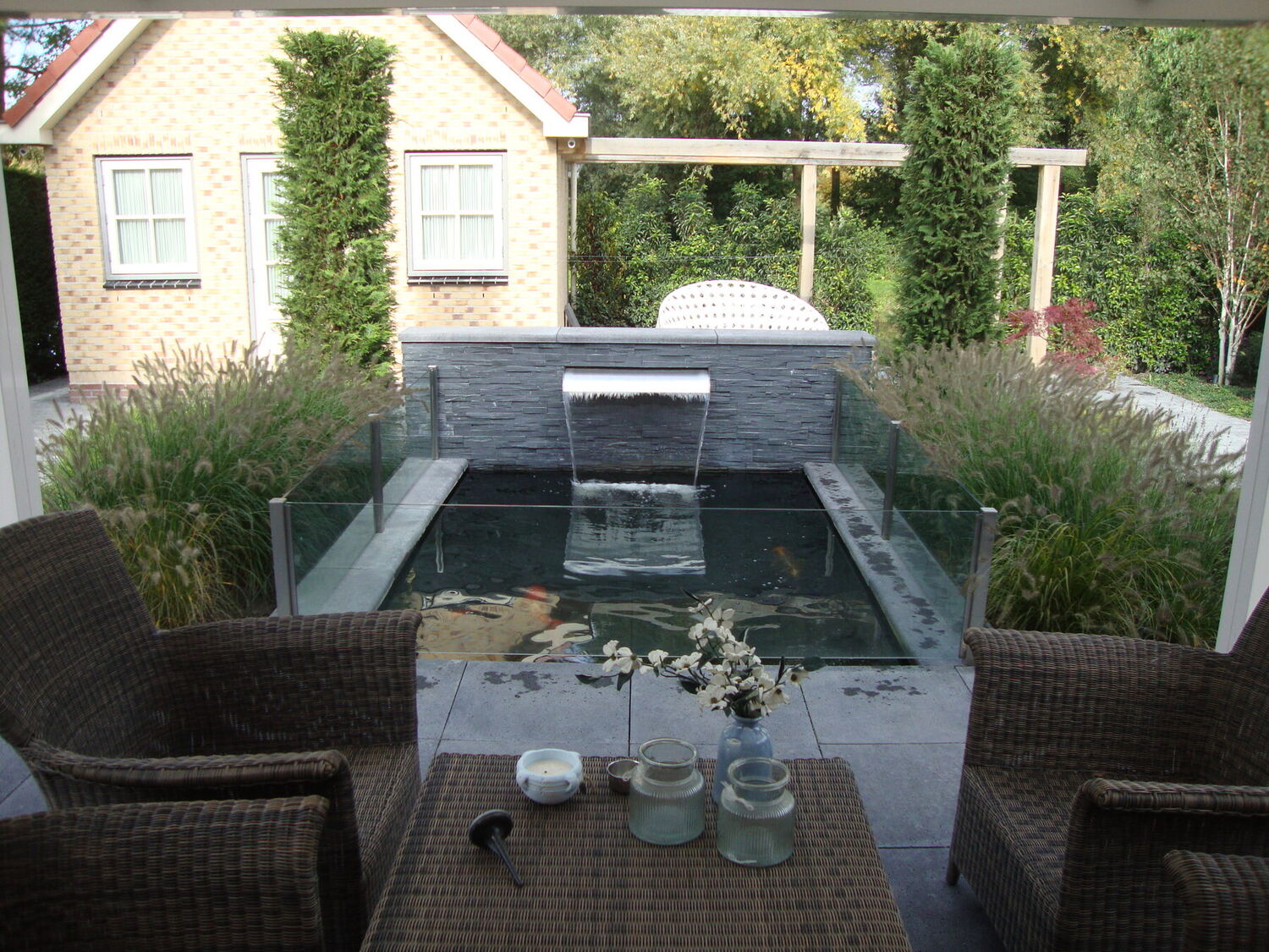 Strakke vijver met waterval en terras in een particuliere tuin